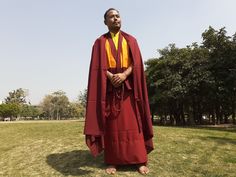 a man standing in the grass wearing a red and yellow monk outfit with his hands folded