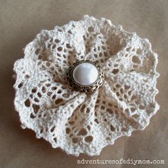 a white crocheted doily with a pearl brooch on it's center