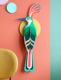 a colorful bird clock mounted to the side of a wall next to a yellow chair