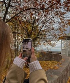 a woman taking a photo with her cell phone in front of a gazebo on a fall day