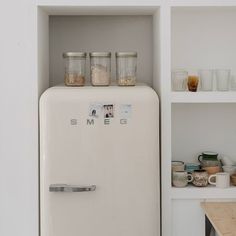 an old refrigerator with jars on top of it in a white kitchen filled with dishes