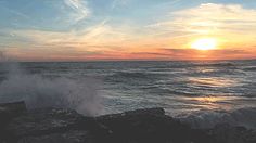 the sun is setting over the ocean with waves crashing on rocks and water splashing against it