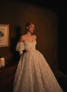 a woman in a white dress standing next to a dresser with candles on the table