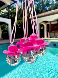 three disco balls hanging from a pink ribbon by the pool in front of a house