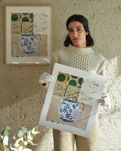 a woman holding up a painting in front of a wall