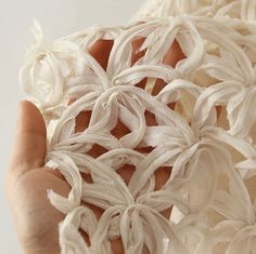 a person holding something made out of yarn with white flowers on it's fingers