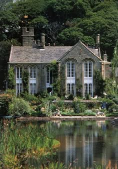 a large house sitting on top of a lush green hillside next to a lake and forest