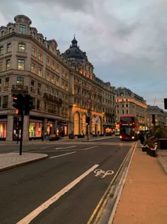 a double decker bus driving down a street next to tall buildings and traffic lights at dusk