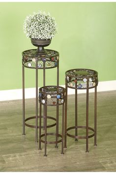 three metal tables with flowers on them in front of a green wall and wooden floor