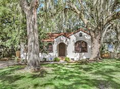 a white house surrounded by trees with spanish moss hanging from the roof and green grass