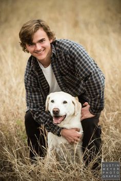 a man kneeling down with his dog in the middle of a grassy field and smiling