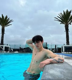 a shirtless man sitting on the edge of a swimming pool next to palm trees