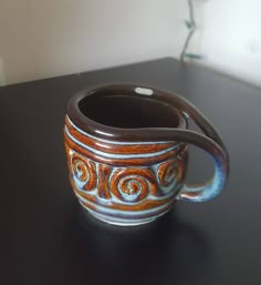 a brown and blue cup sitting on top of a black table next to a vase