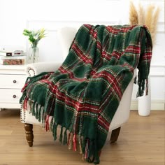 a green and red plaid blanket sitting on top of a chair next to a vase