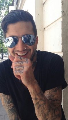 a man with tattoos and piercings on his face is holding his hands to his mouth