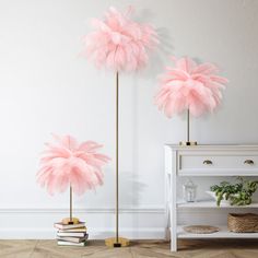 two tall pink ostrich feather lamps on gold bases in front of a white wall