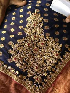 a person is sewing on a piece of cloth with gold and red flowers in it