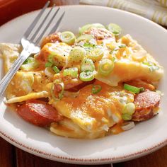 a white plate topped with cheesy pizza covered in cheese and vegetables next to a fork