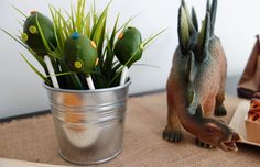 two dinosaur figurines sitting next to each other near a tin can filled with carrots