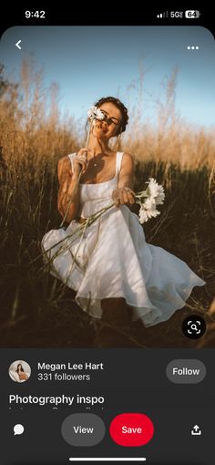 a woman in a white dress holding flowers and taking a selfie with her cell phone