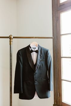 a tuxedo is hanging on a clothes rack in front of a window,