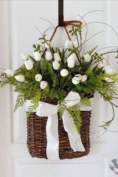 a wicker basket with white flowers and greenery hanging from the front door handle