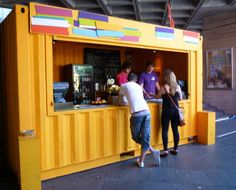 some people are standing at a yellow food stand and one person is ordering from the counter