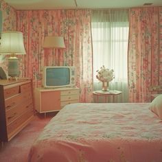 a bedroom with floral wallpaper and pink bedspread, dressers, lamps, and television