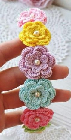 crocheted flower brooch pins in different colors and sizes are shown on someone's hand