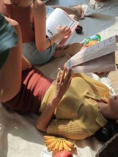 two women are sitting on the ground reading books and eating fruit while one looks at her phone