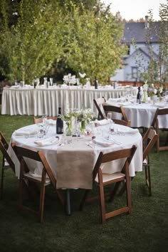 an outdoor dining area with tables and chairs covered in white tablecloths, surrounded by trees