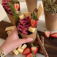 a person is holding up some food in their hand with strawberries and cheese on the side