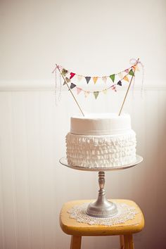 a white cake sitting on top of a wooden table next to a yellow chair and wall