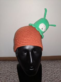 a crocheted hat with a green and orange creature on it's head