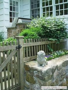 a dog statue sitting on top of a stone bench in front of a wooden fence