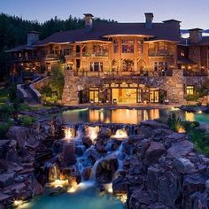 a large house with a waterfall in front of it and lights on the water below