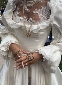 a woman with tattoos on her arms and hands wearing a white dress, holding onto an arm