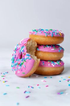 three donuts with pink frosting and sprinkles are stacked on top of each other