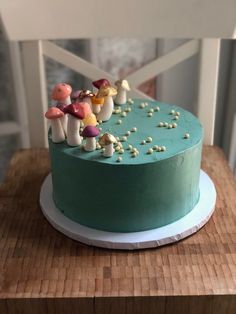 a green cake with mushrooms on it sitting on a wooden table next to a white chair