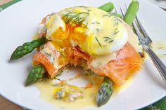 a white plate topped with salmon and asparagus covered in hollandaise sauce