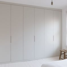 an empty bedroom with white walls and cabinets in the corner, along with a small wooden bench