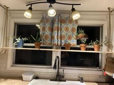 a kitchen window with potted plants on the ledge and lights hanging from the ceiling