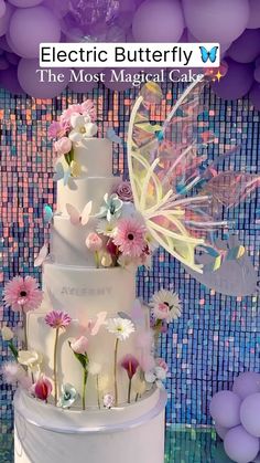 there is a wedding cake with flowers on the top and butterflies on the bottom, along with balloons in the background