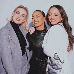 three women standing next to each other in front of a white wall