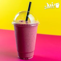 a smoothie in a plastic cup on a pink and yellow surface with a straw