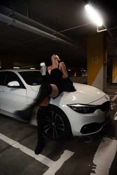 a woman sitting on the hood of a white car holding a drink in her hand