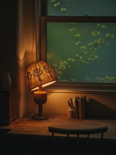 a lamp sitting on top of a wooden table next to a window with green leaves