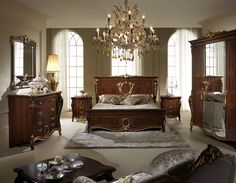 a bedroom with a chandelier, bed and dressers in front of two windows