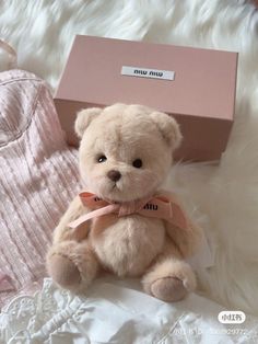 a teddy bear sitting on top of a white blanket next to a pink gift box