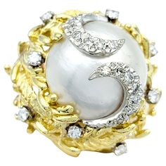 Ring size: 5.75 This captivating cocktail ring, a grand statement of opulence and artistry, showcases a cultured cabochon center pearl with luminescent white hues, delicately adorned with subtle silver overtones. The pearl's pristine elegance is gracefully cradled within an 18 karat yellow gold dome setting, which adds an air of regal warmth to the piece. The meticulously crafted detailing on the ring's surface resembles intricate leaf and twig motifs, as if the pearl is sitting in an ornate nes Pearl Cocktail Ring, Pearl Diamond, Pearl Color, Silver Pearls, Baroque Pearls, White Diamonds, Cocktail Ring, Diamond Clarity, Cultured Pearls